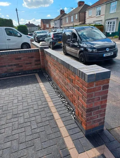 Charcoal block paving drive with buff band beside a new brick wall after completion