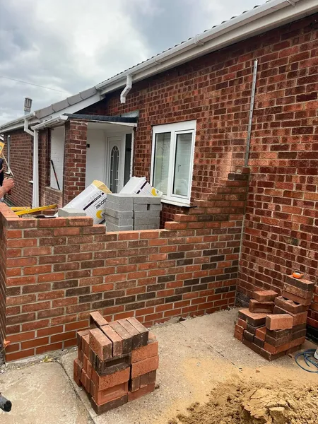 Extension brick walls being built round a rear doorway with bricks stacked ready