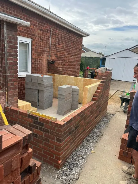 Low brick extension walls going up with concrete blocks stacked inside during construction