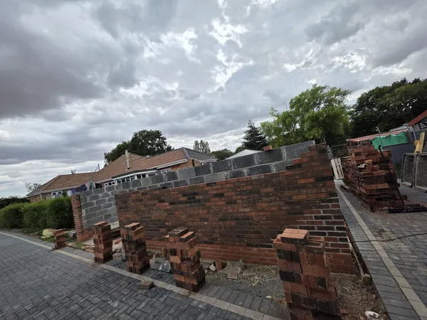 New brick garden wall rising on a block paved drive during brickwork