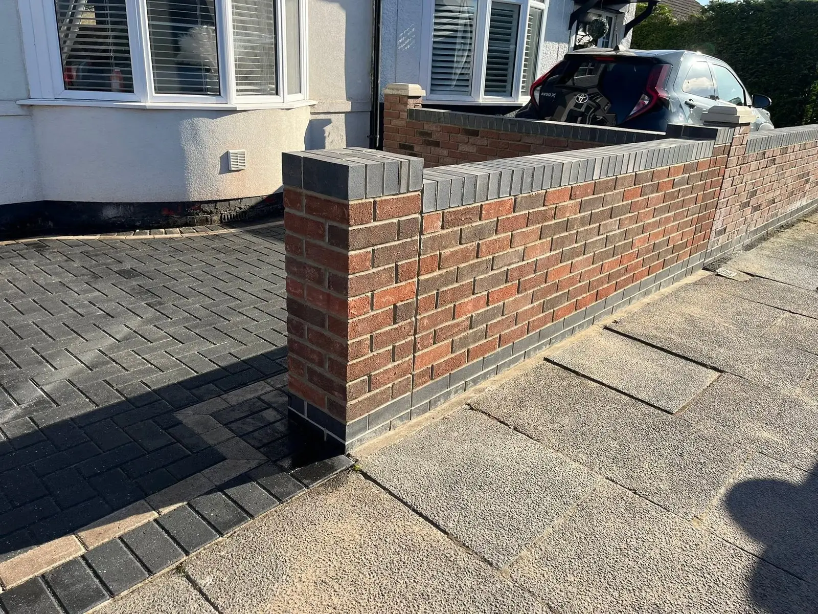 New brick front wall with charcoal coping beside block paving after completion