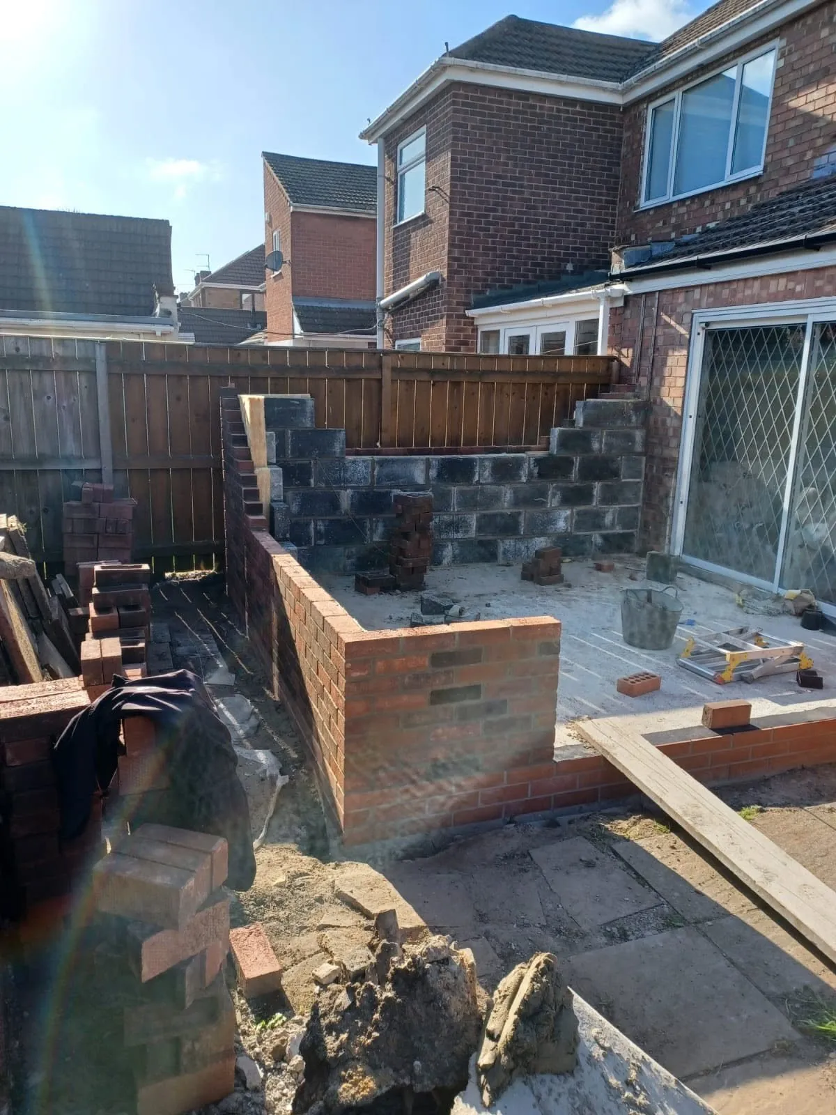 New red brick garden walls being built on the new foundation beside patio doors