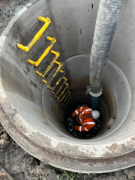 Worker at the bottom of a deep concrete manhole shaft with yellow step irons