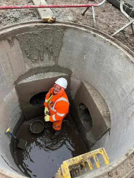 Worker standing in a concrete drainage manhole with benching and pipe openings