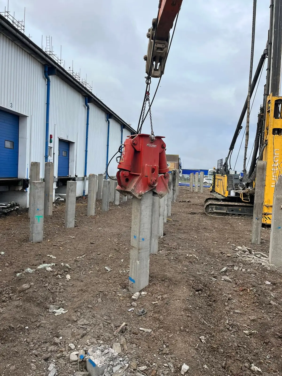 Pile cropper on concrete piles beside a yellow piling rig at a warehouse