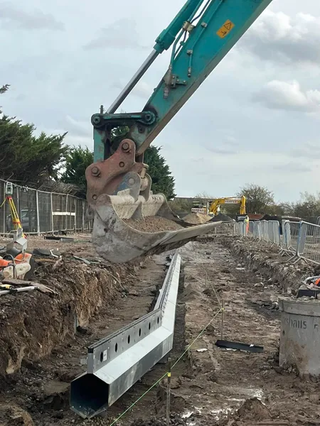 Steel slot drain run in a gravel bed trench with an excavator behind