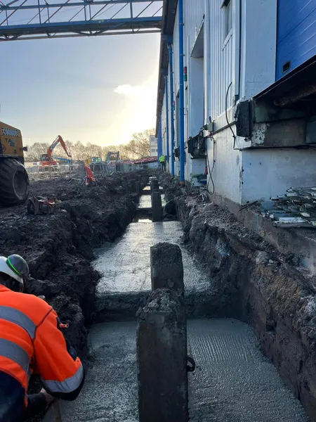 Fresh concrete footings poured in a trench along an industrial unit wall