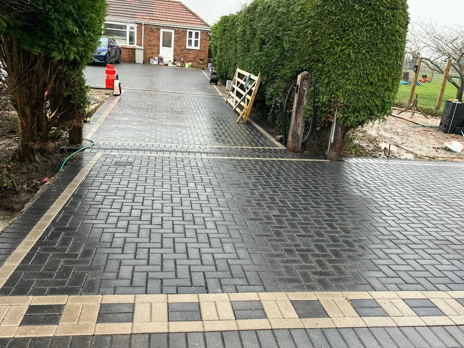 Long charcoal block paving drive with a buff border band after completion