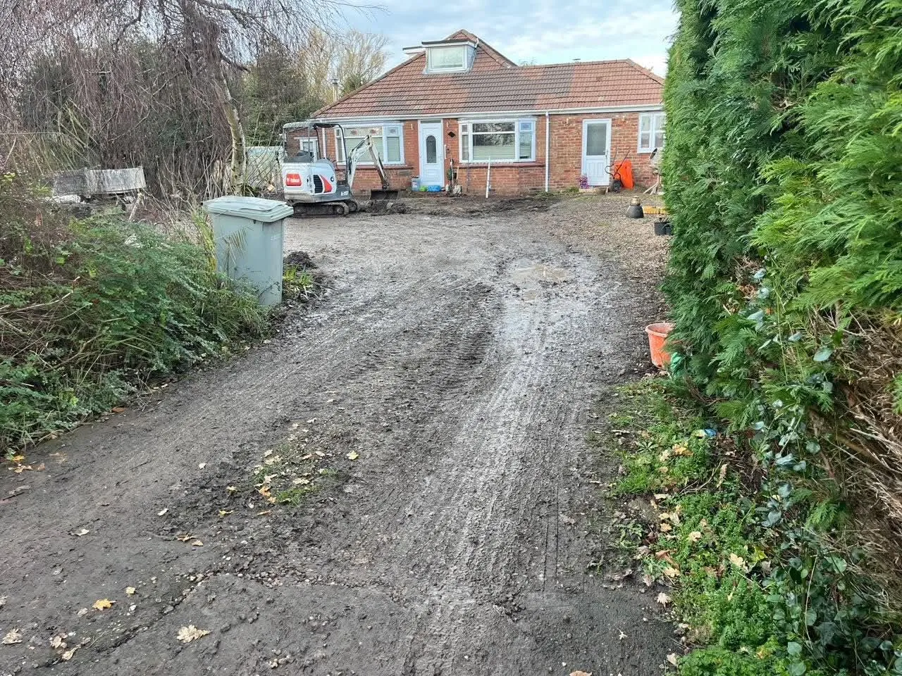 Muddy track between hedges before a new long block paving driveway