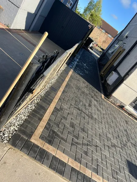 Charcoal block paving side drive with a buff border beside a house