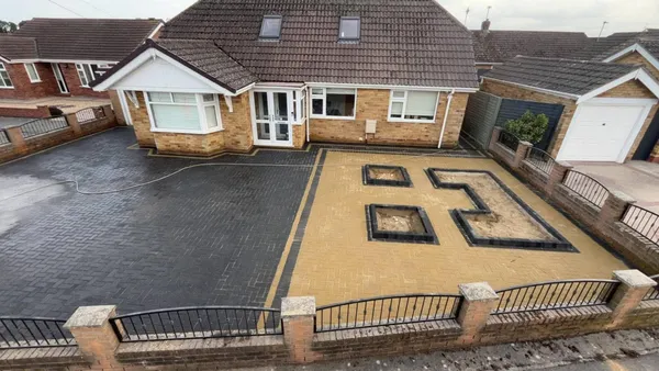 Finished buff and charcoal block paving drive with step block planters by a bungalow
