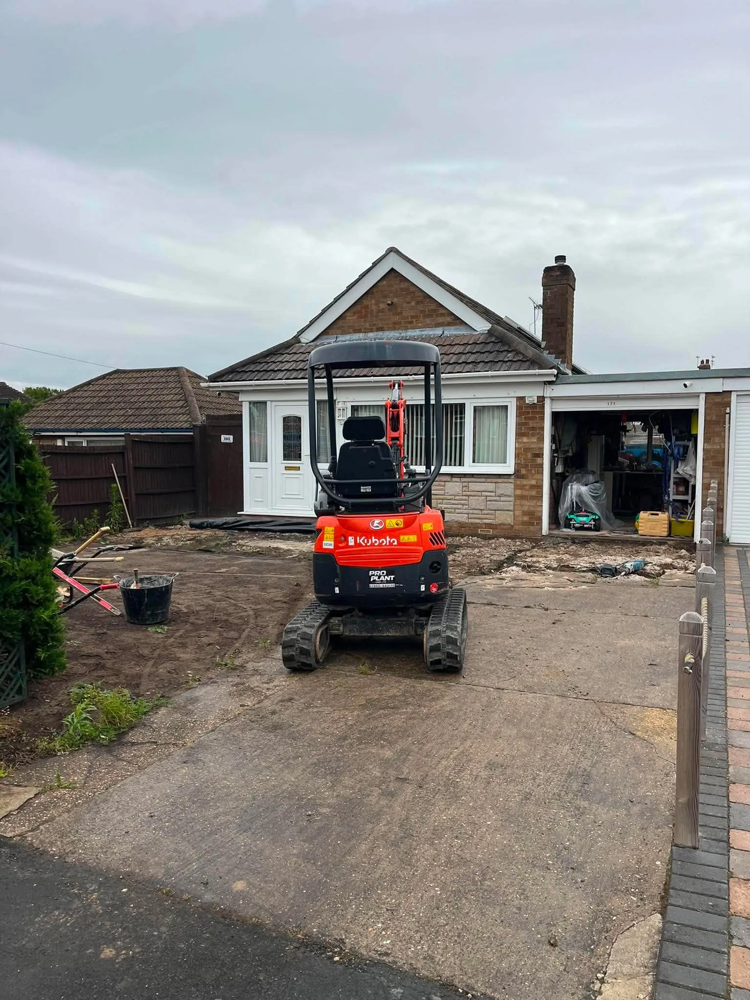 Old concrete drive with mini digger before new bordered concrete driveway