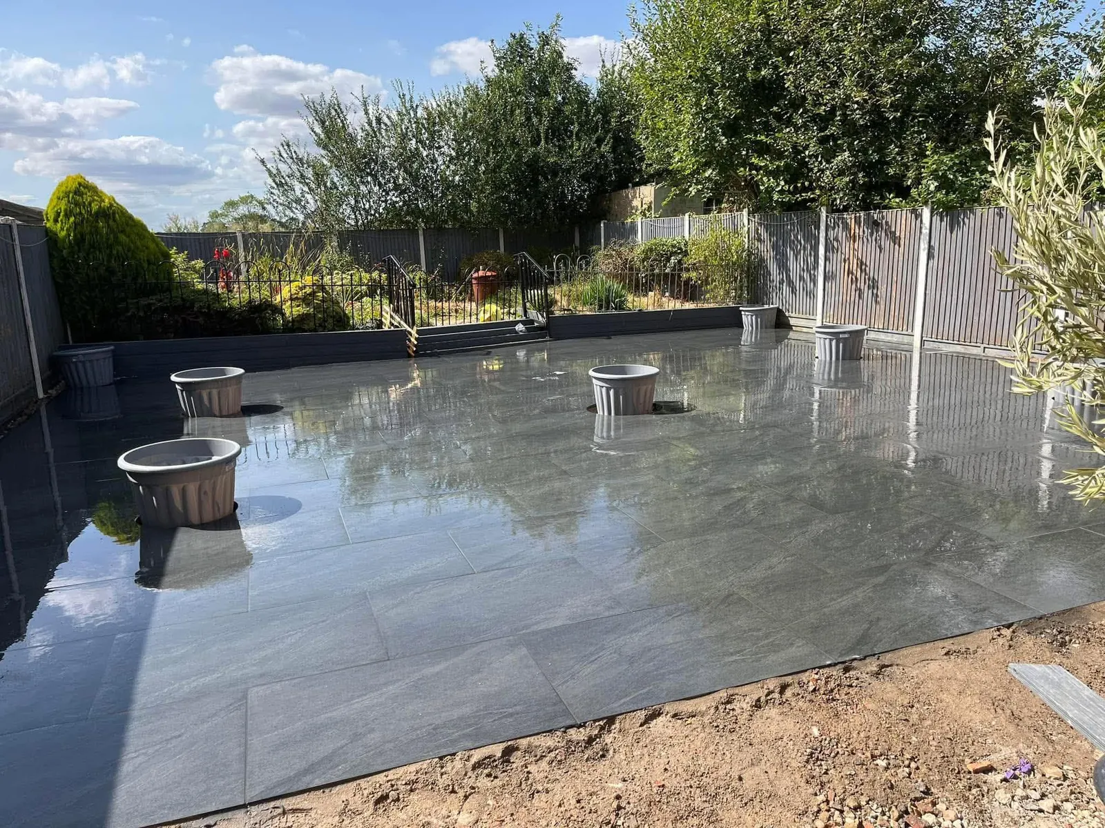 Dark grey porcelain patio with round planters in a fenced rear garden after completion