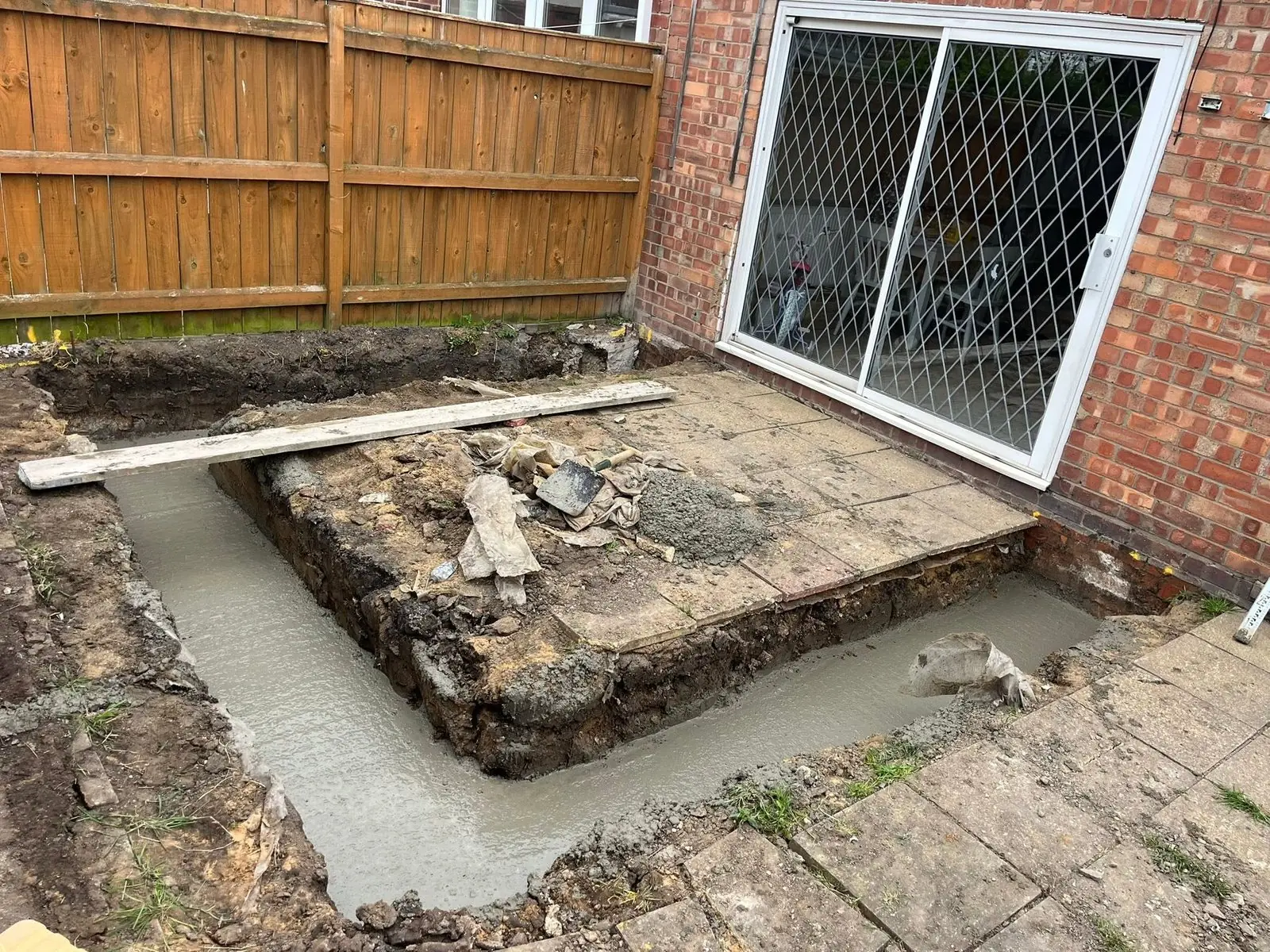 Concrete strip foundation poured in a trench beside patio doors for a new garden wall