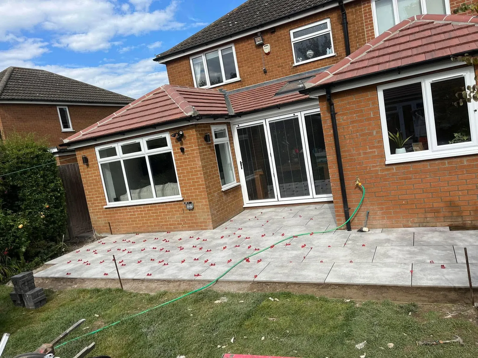 Grey porcelain patio slabs being laid with clips during installation at a brick house