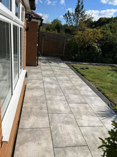 Grey porcelain patio along white framed doors with lawn after completion