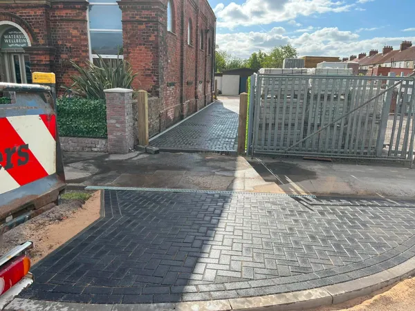 Charcoal block paving entrance with a curved border beside a brick building after completion