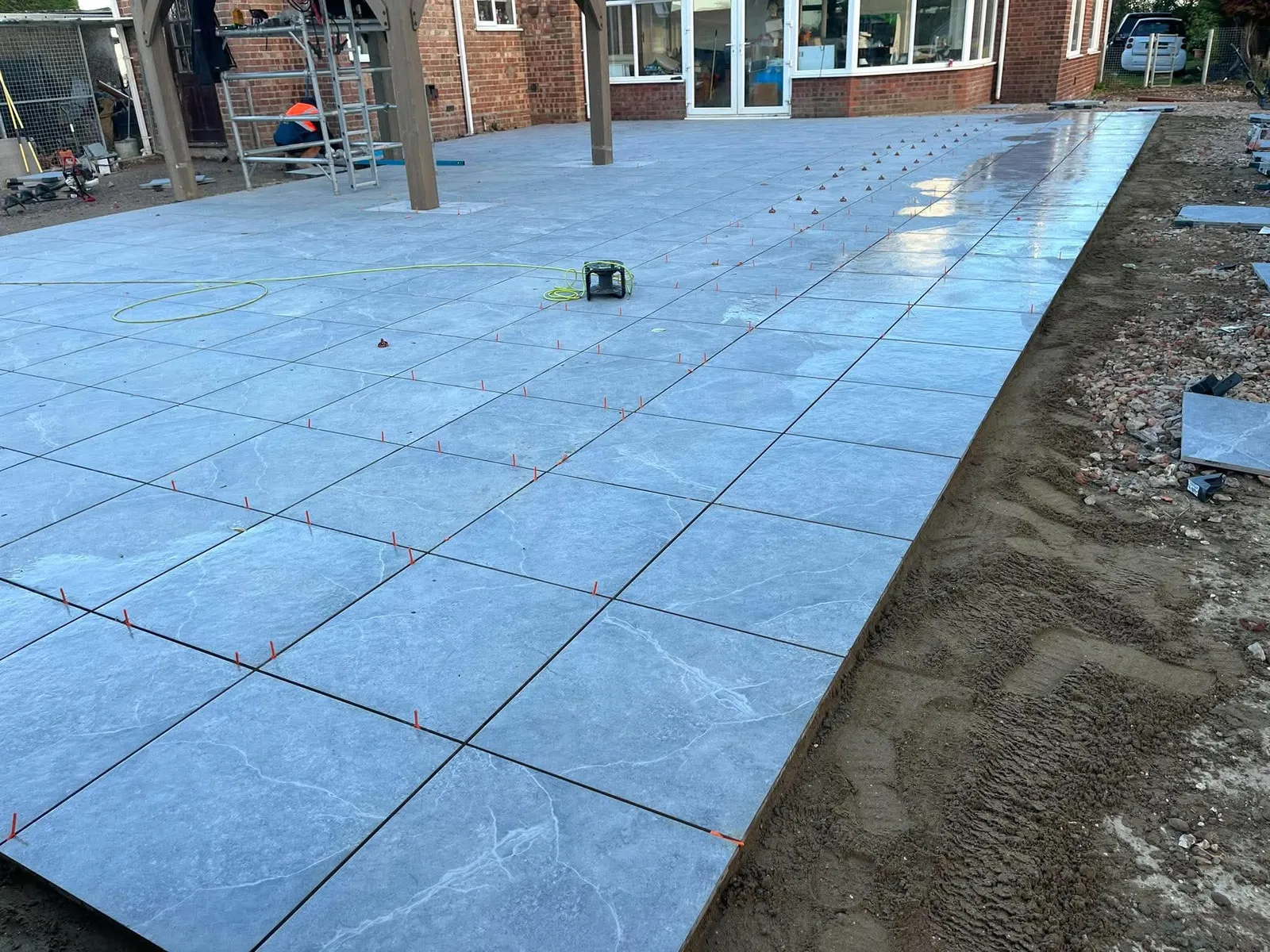 Large grey porcelain patio freshly laid with gazebo posts during installation