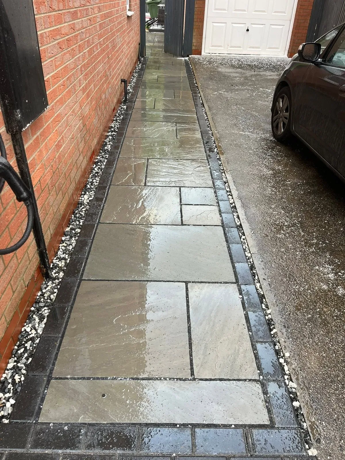 Grey slab side path with charcoal block border beside a driveway after completion