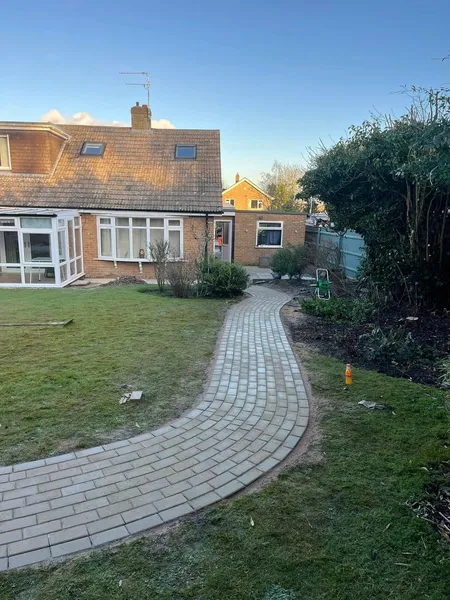 Curved grey block paving garden path across a rear lawn