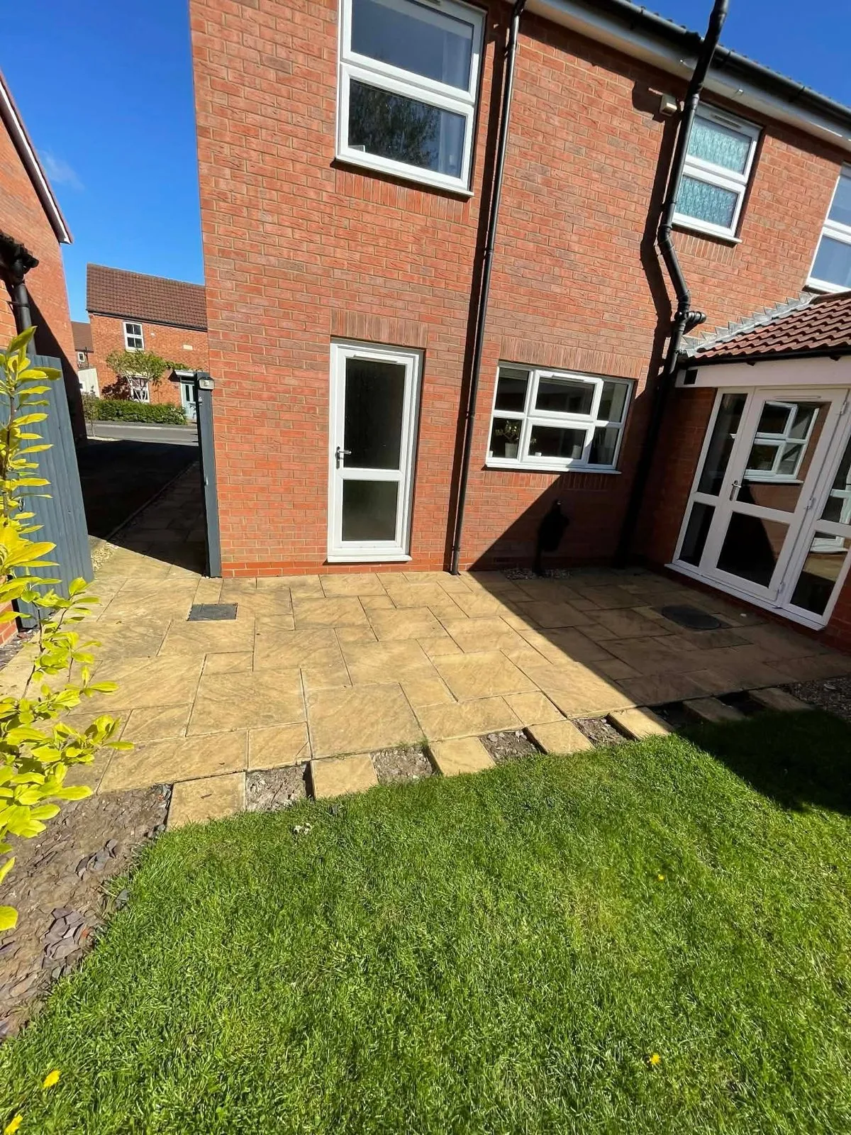 Old buff patio slabs beside a lawn at a brick house before replacement