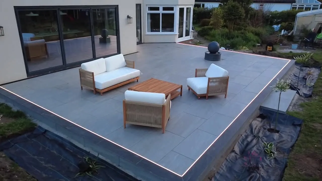 Raised grey porcelain patio with LED edge lighting and garden furniture at dusk
