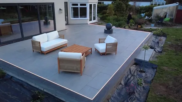 Raised grey porcelain patio with lit edges, a water feature and an outdoor sofa set
