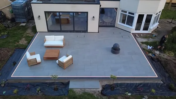 Aerial view of a raised porcelain patio with LED lit edges behind a rendered house
