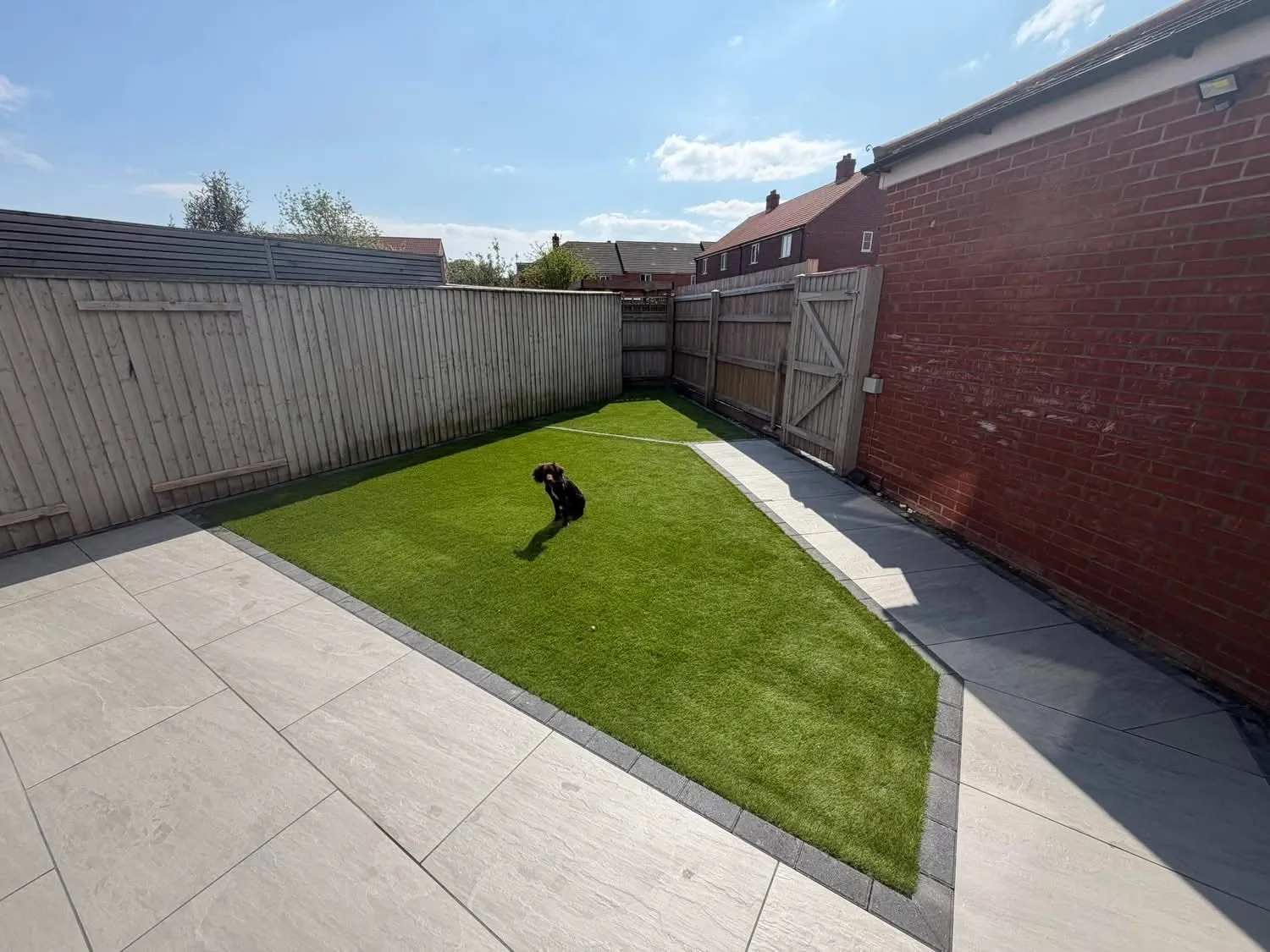 Artificial grass laid beside a grey porcelain patio after completion