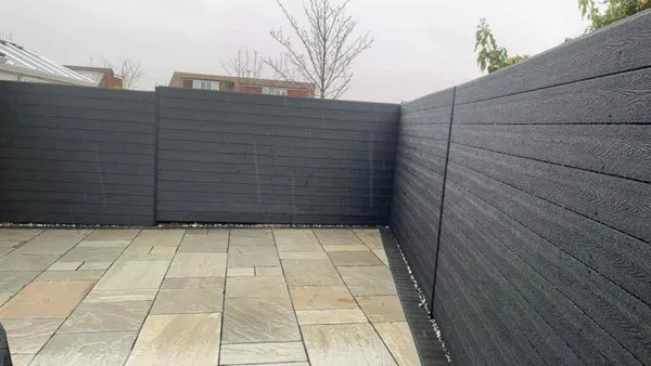 Dark grey composite fencing around a buff sandstone patio after completion