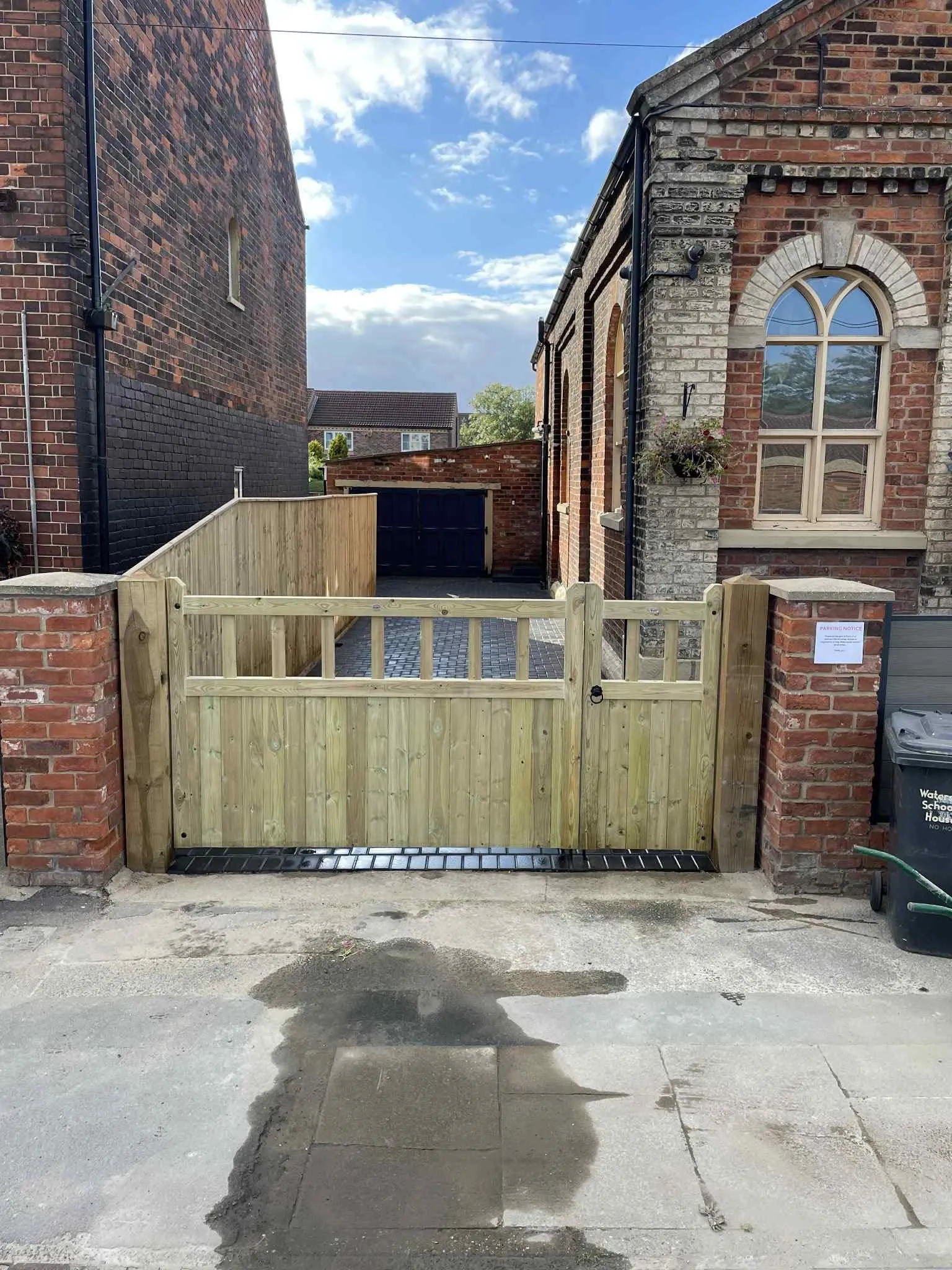 Wooden double driveway gates hung between red brick pillars