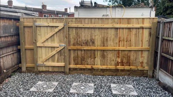 Close board wooden fence and ledged gate above gravel with patterned stepping slabs