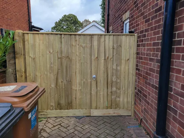 Timber close board gate above red block paving beside a brick house after completion