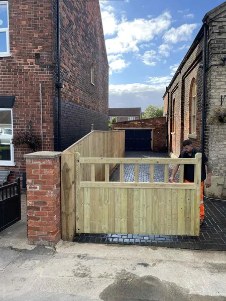 Wooden driveway gate hung on a brick pillar with block paving behind after completion