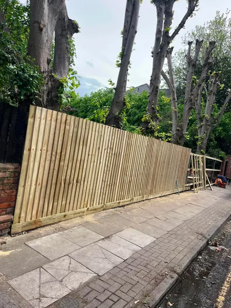 New close board wooden fence along a paved path by trees after completion