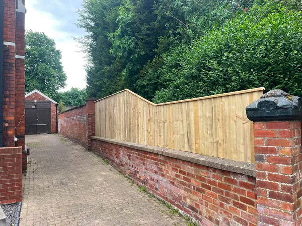 Close board wooden fence on an old brick wall along a paved lane after completion